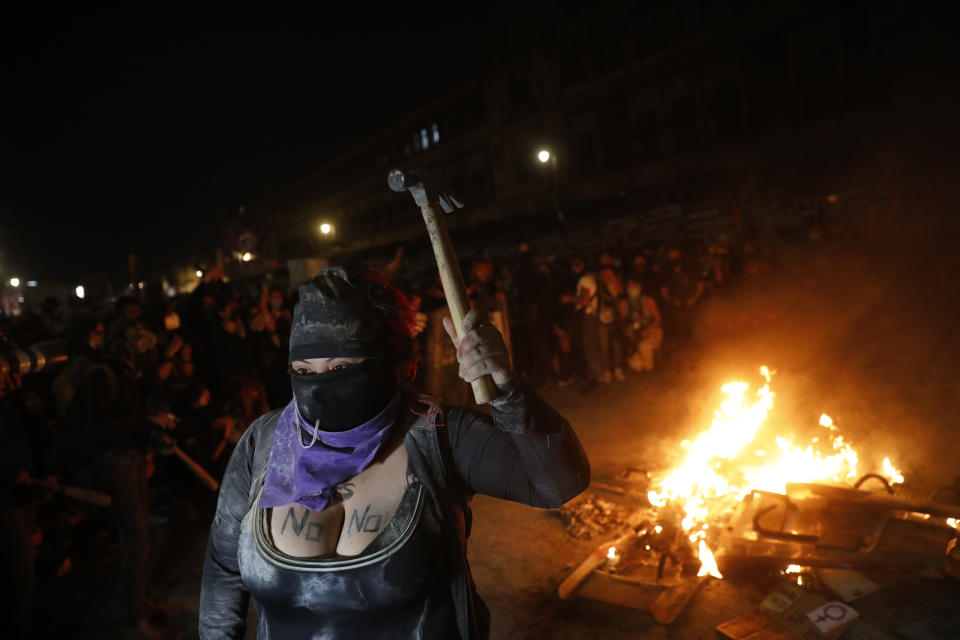 A demonstrator brandishes a hammer as other light a fire in front of the National Palace during a march to commemorate International Women's Day and protesting against gender violence, in Mexico City, Monday, March 8, 2021. (AP Photo/Rebecca Blackwell)