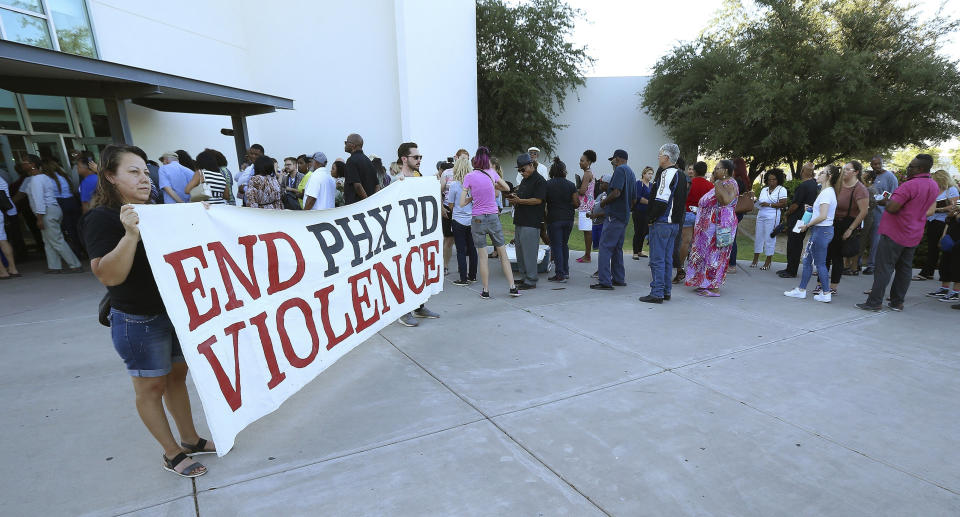 FILE - In this June 18, 2019 file photo people line up near protesters outside a venue for a community meeting in Phoenix. Still stinging from national outrage sparked this summer by a videotaped encounter of officers pointing guns and cursing at a black family, community members are holding low-key meetings aimed at helping Phoenix officials figure out how citizens could help oversee the city's officers. (AP Photo/Ross D. Franklin, File)