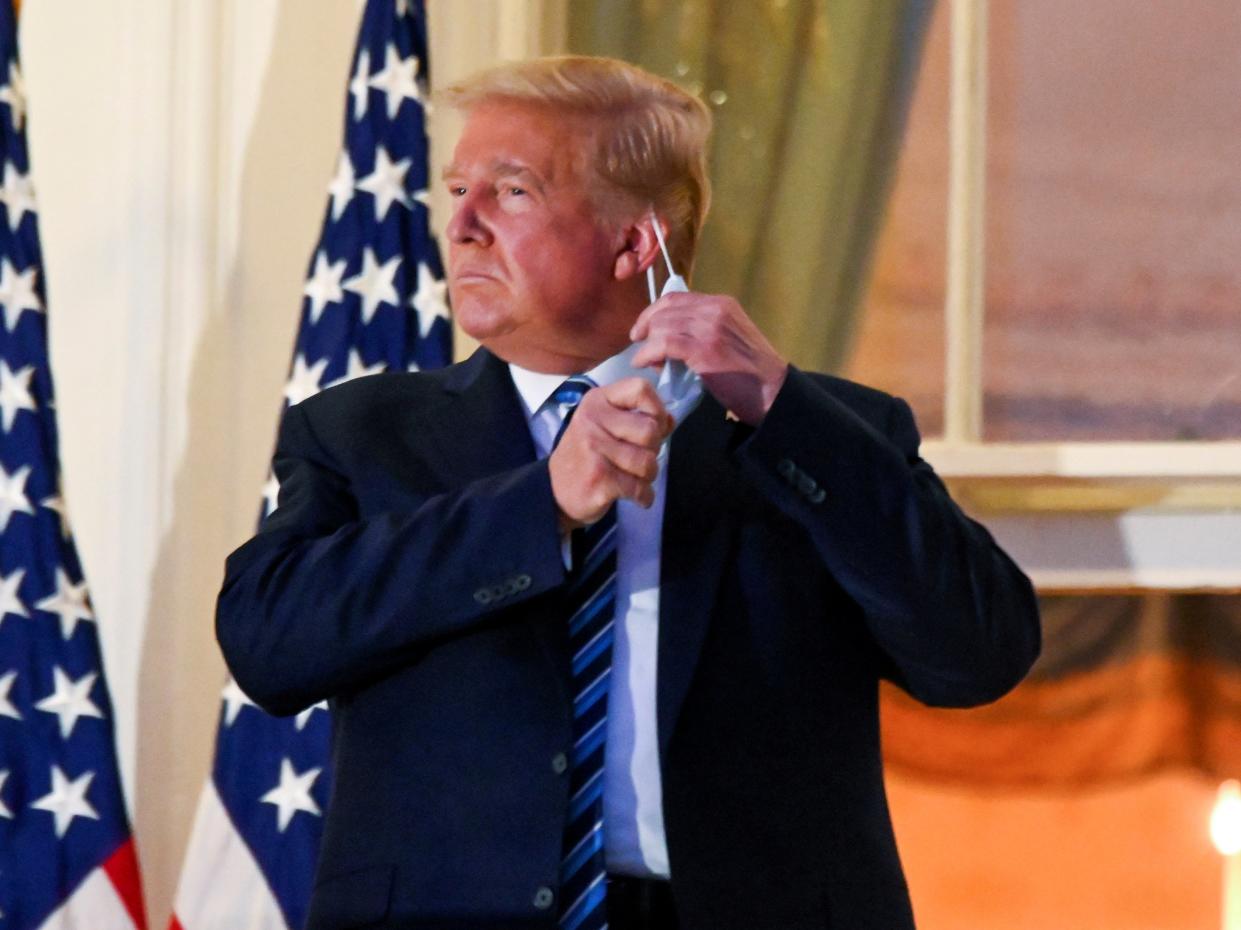 Donald Trump pulls off his protective face mask at the White House after returning from Covid treatment at Walter Reed Medical Center on 5 October, 2020 (REUTERS)