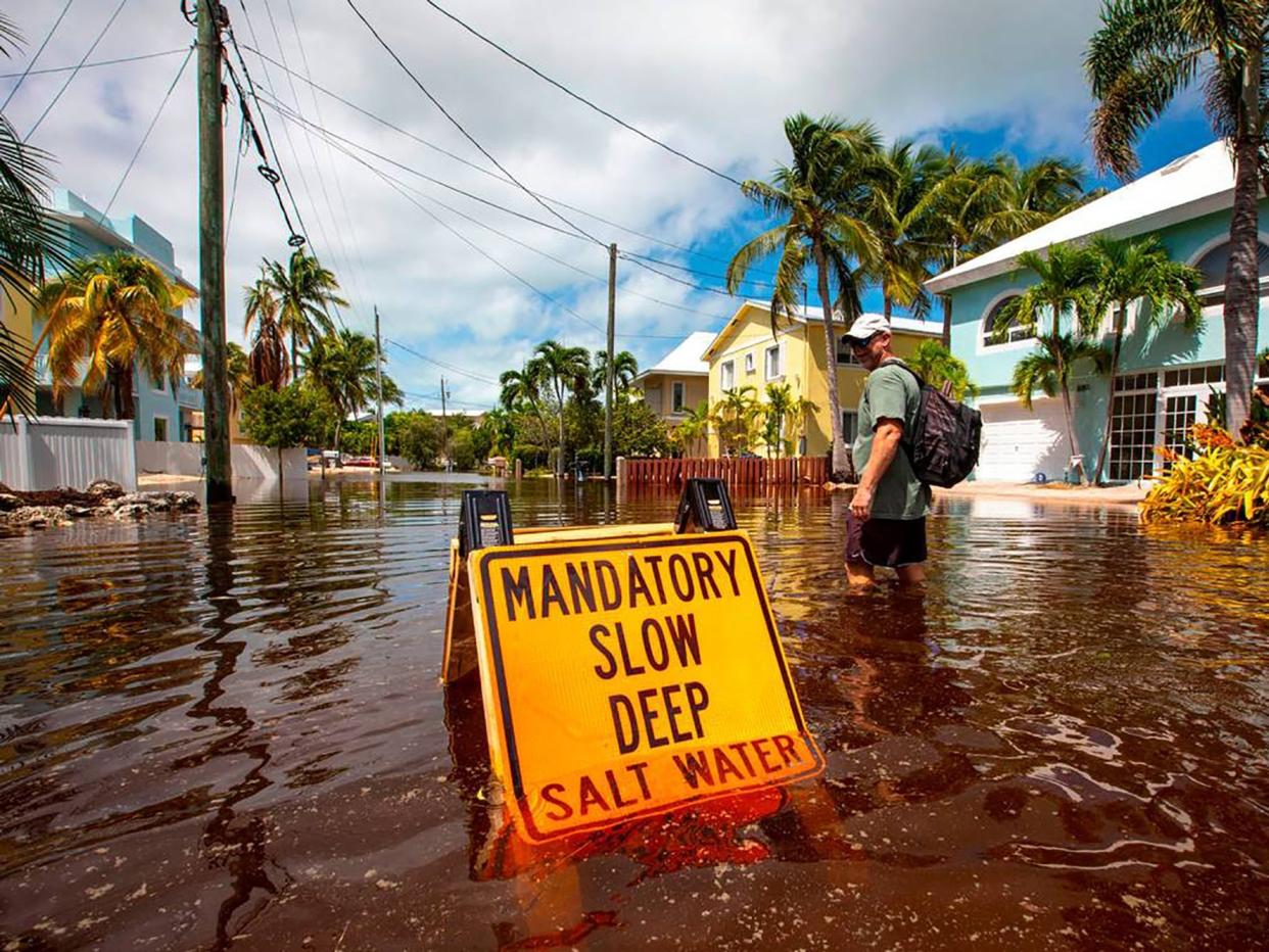 A Florida road flooded during Hurricane Ian during a sunny day, with a yellow sign that reads "Mandatory slow deep salt water."