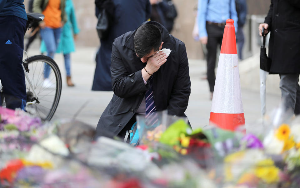 A man reacts next to floral tributes for the victims