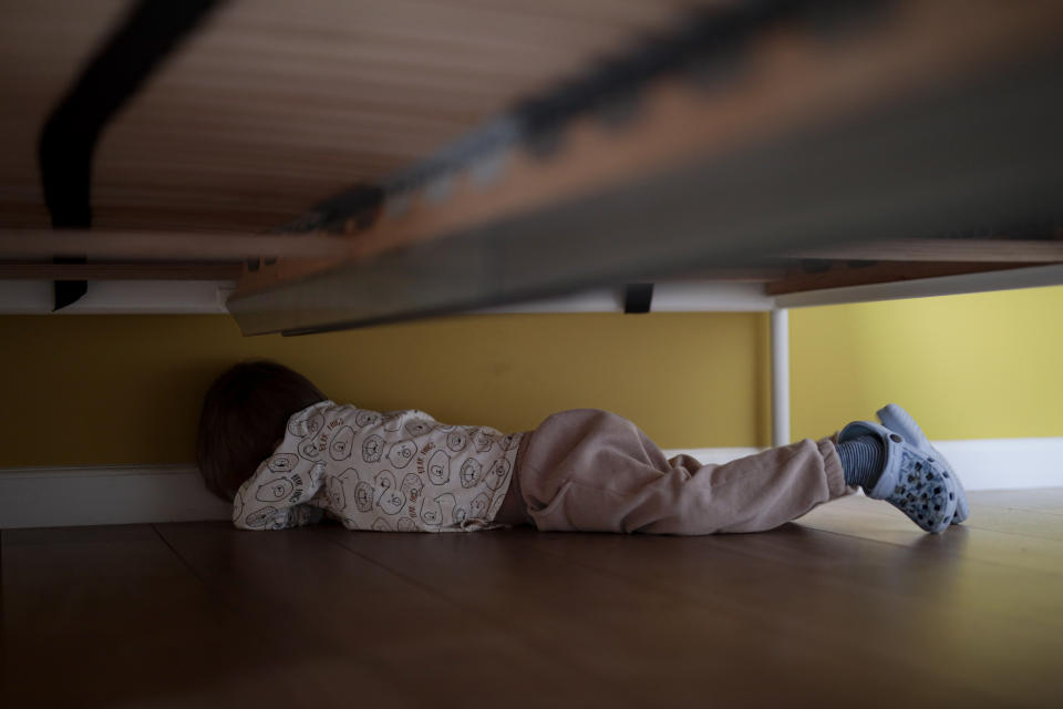 Timofey, 3 years old, hides under the bed during an interview with The Associated Press, in Brasov, Romania, Wednesday, March 30, 2022. Having escaped from Russian shelling, Ukrainian refugees are now focused on building new lives — temporarily or permanently. Countries neighboring their homeland, like Poland and Romania, are sparing no effort to help them integrate and feel needed in the new environment. (AP Photo/Stephen McGrath)