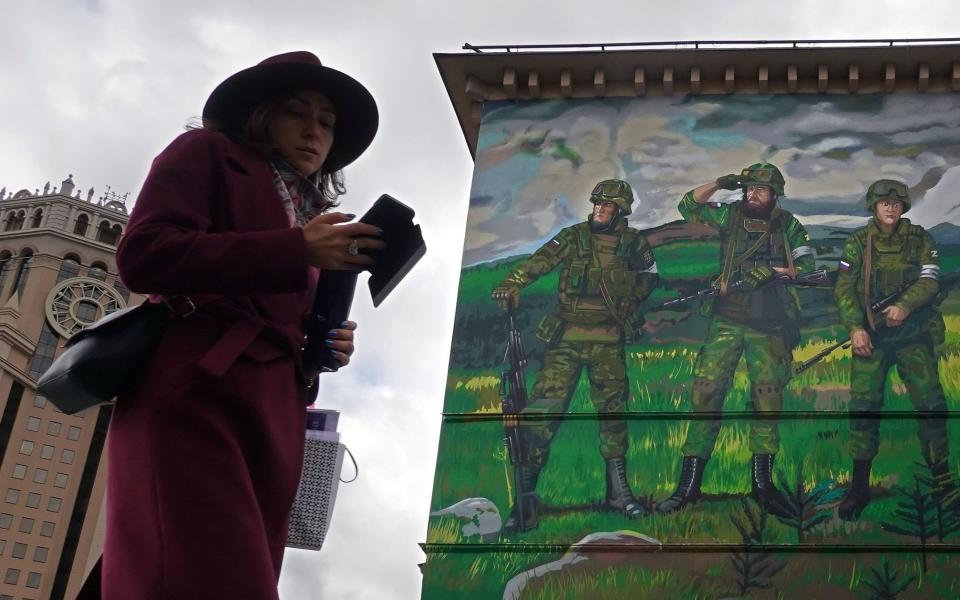 A woman using a mobile phone walks in front an apartment block decorated with a mural in support of Russia's army 'special military operation' in Ukraine, in Moscow - Shutterstock/ MAXIM SHIPENKOV/EPA-EFE