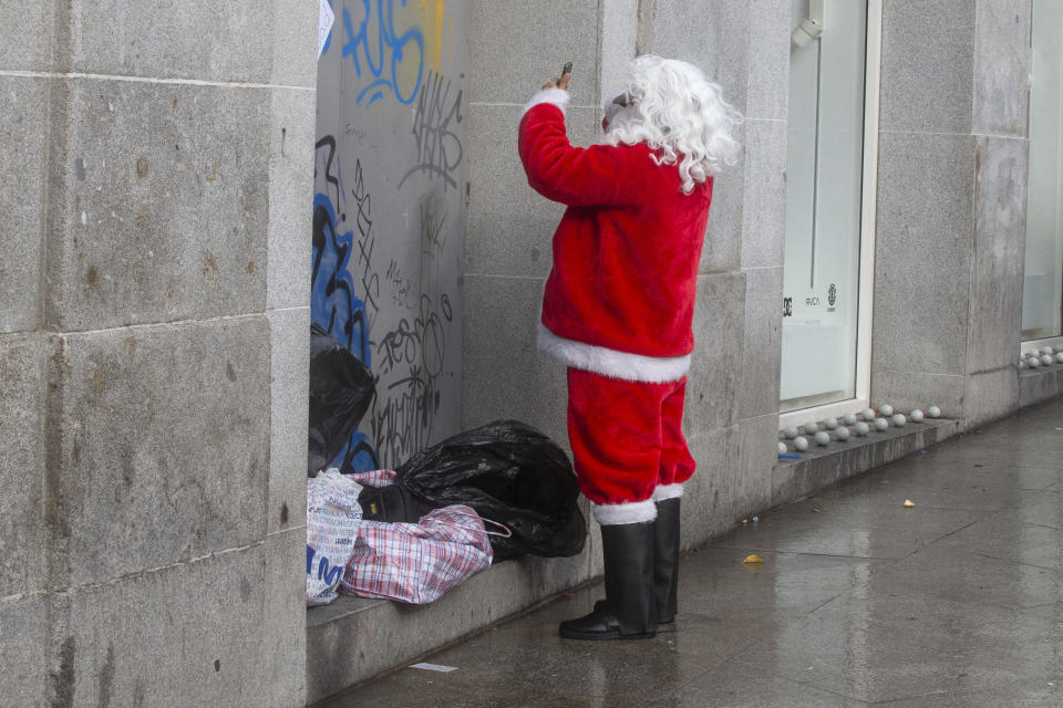 A man dressed as Santa Claus, adjusts his wig looking through the selfie mode on his phone in Madrid, Spain, Saturday, Dec. 21, 2019. People in costumes pose for photos with tourist for money. (AP Photo/Paul White)