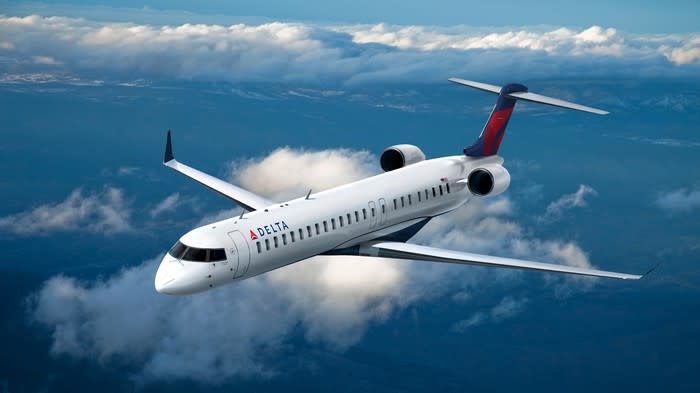 A Delta Air Lines regional jet flying over a cloud.