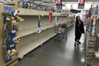 A woman shops near empty shelves at a Hy-Vee food store Friday, March 13, 2020, in Overland Park, Kan. (AP Photo/Charlie Riedel)