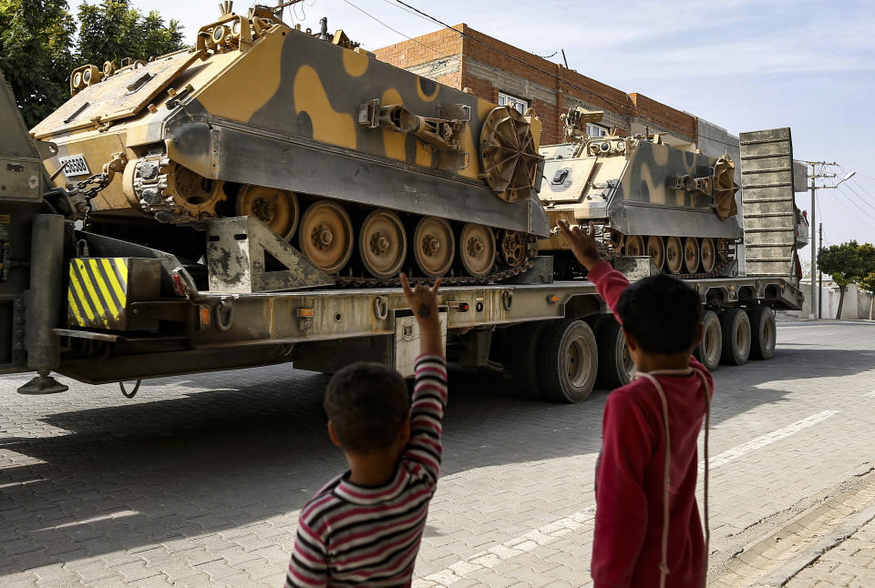 Children wave to a Turkish forces truck transporting armoured personnel carriers at the border with Syria in Karkamis, Gaziantep province, southeastern Turkey, Tuesday, Oct. 15, 2019. Turkey defied growing condemnation from its NATO allies to press ahead with its invasion of northern Syria on Tuesday, shelling suspected Kurdish positions near the border amid reports that Syrian Kurds had retaken a key town. (AP Photo/Emrah Gurel)