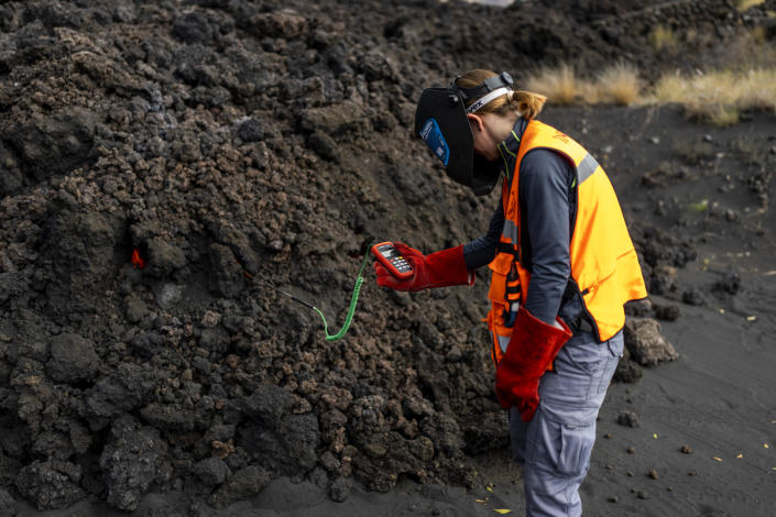 A scientist with the Canary Islands' volcanology institute, Involcan, measures the temperature of a lava flow on the Canary island of La Palma, Spain, Saturday, Oct. 30, 2021. Scientists from around the world flocking to an eastern Atlantic Ocean island are using an array of new technologies available to them in 2021 to scrutinize — from land, sea, air, and even space — a rare volcanic eruption. But despite technological and scientific leaps, predicting volcanic eruptions and, more crucially, how they end, remains a mystery. (AP Photo/Emilio Morenatti)