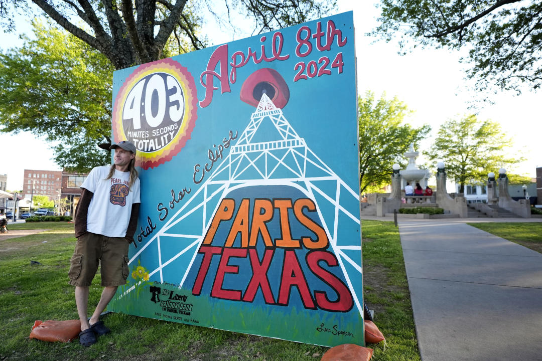 Una persona si sporge sul cartello che legge: 4:03 minuti e un secondo intero, 8 aprile 2024, eclissi solare totale, Parigi, Texas.