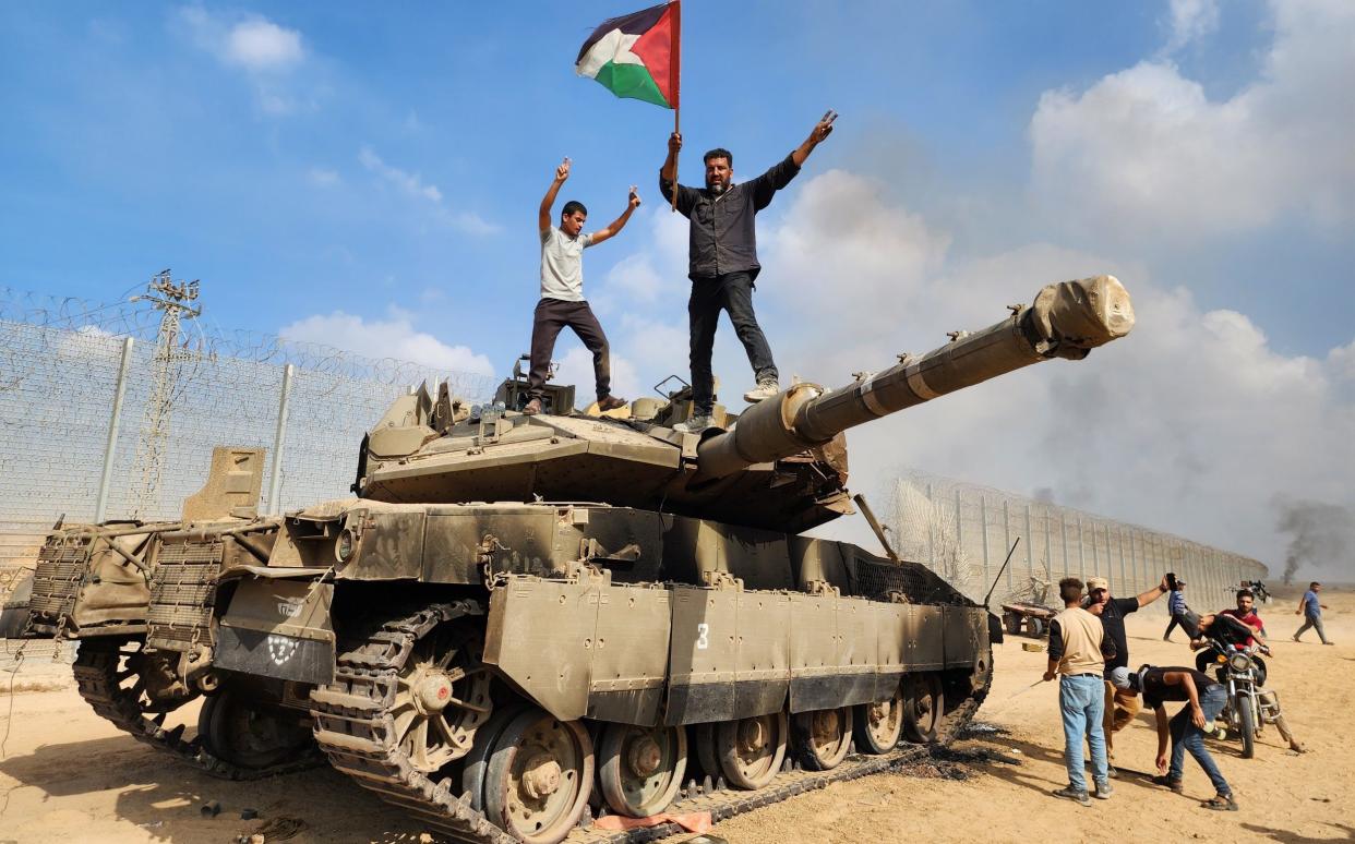 Members of Hamas's military wing, the Izz ad-Din al-Qassam Brigades, stand atop a destroyed Israeli tank in Gaza