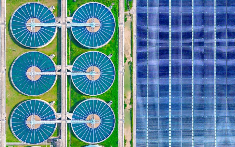 An overhead view of 6 round water treatment tanks at a large water treatment facility next to solar panels.