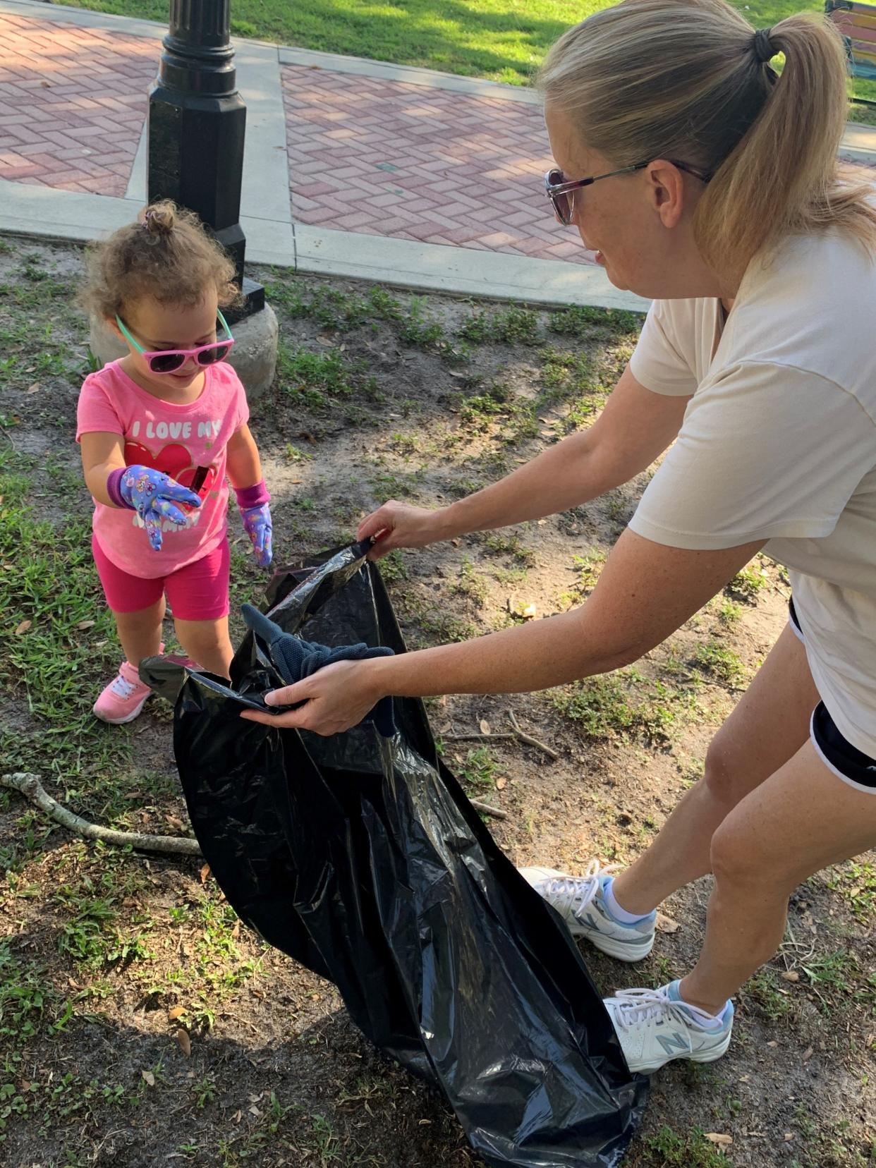 Lilly Arjoon, 2, drops a bottle cap into a trash bag as she helps her grandmother, Chris Myers, pick up trash in Cocoa Village.