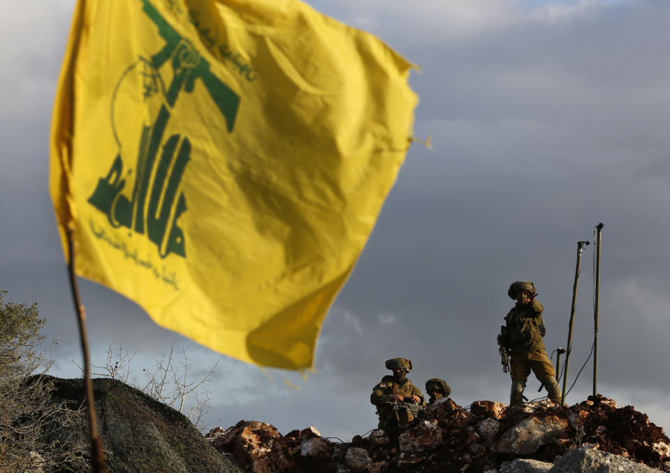 In this Thursday, Dec. 13, 2018 photo, Israeli soldiers stand guard next to cameras at their new position in front of a Hezbollah flag, near the Lebanese southern border village of Mays al-Jabal, Lebanon. As Israeli excavators dig into the rocky ground, Lebanese across the frontier gather to watch what Israel calls the Northern Shield operation aimed at destroying attack tunnels built by Hezbollah. But Lebanese soldiers in new camouflaged posts, behind sandbags, or inside abandoned homes underscore the real anxiety that any misstep could lead to a conflagration between the two enemy states that no one seems to want. (AP Photo/Hussein Malla)