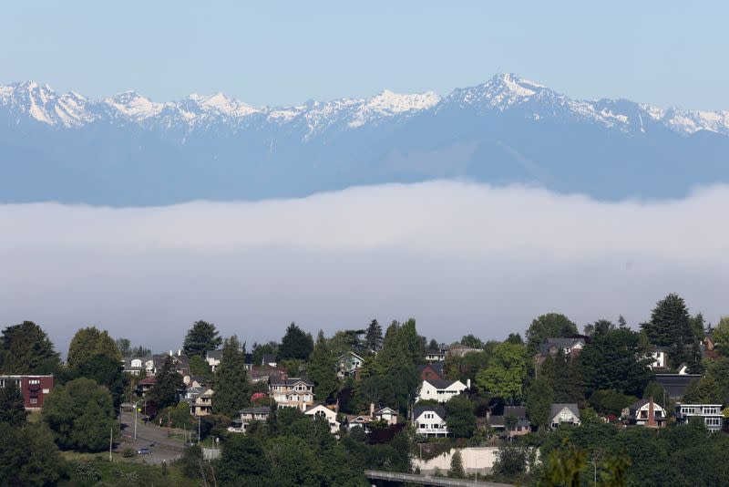 Residential homes are visible under the backdrop of the Olympic Mountains and low fog in the Magnolia neighborhood of Seattle