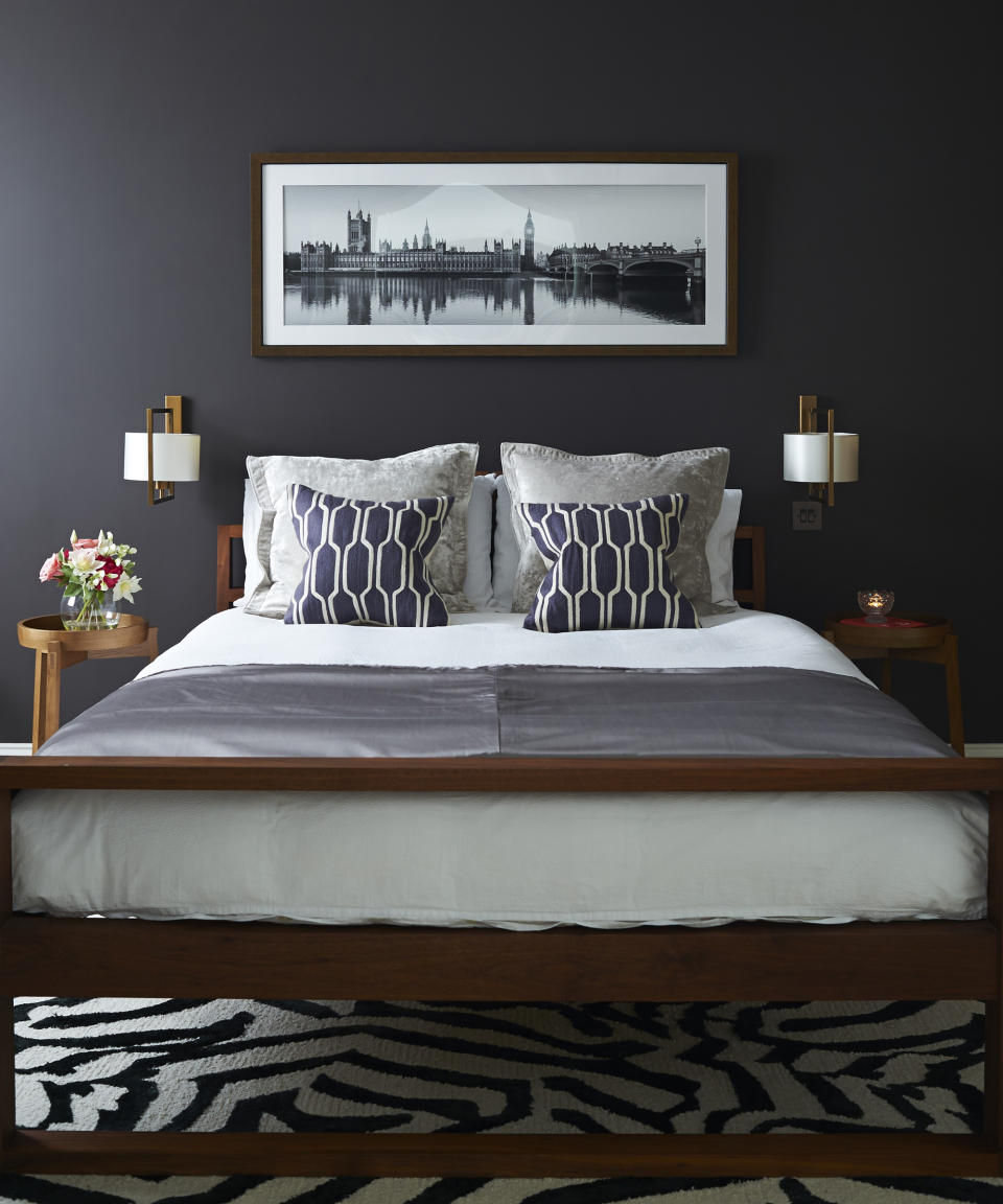 A bedroom with black walls, white and grey bedding, and a black and white graphic rug