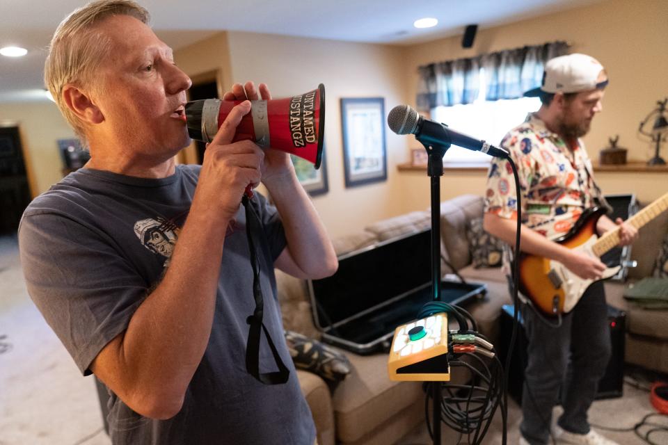 Using a megaphone to sound like the lead singer of The Strokes, Untamed Mustangz vocalist Randy Crome, left, practices alongside guatarist Ryan Bach, right Tuesday afternoon in his basement.