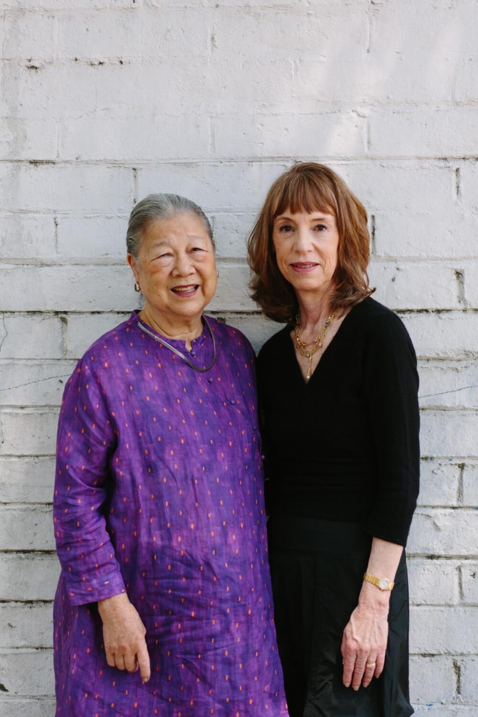 Two women pose for a portrait against a white wall.