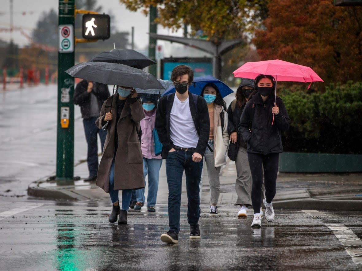 People are pictured with umbrellas and face masks to protect them against the elements and COVID-19 while walking through rain in Vancouver, British Columbia. (Ben Nelms/CBC - image credit)