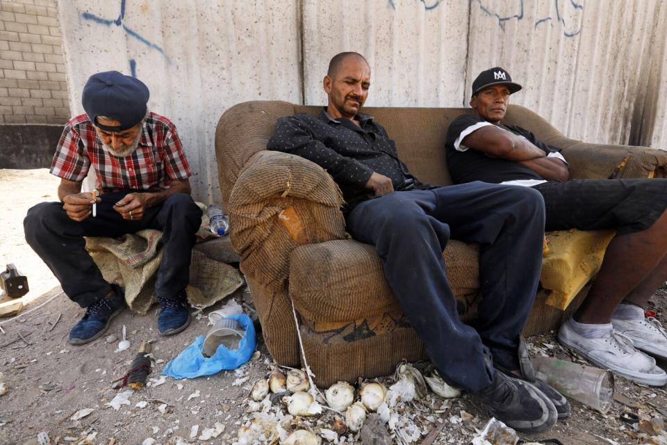 Two men are seated on a couch next to another man, with debris on the ground
