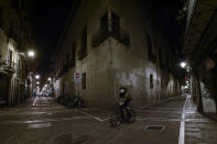 A cyclist wearing face mask protection crosses along an empty High street, in Pamplona, northern Spain, Saturday, Oct. 24, 2020, as new measures against the coronavirus began in the Navarra province where all bar and restaurants are closed for 15 days from midnight Wednesday. (AP Photo/Alvaro Barrientos)