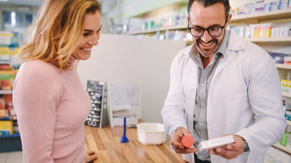 Pharmacist showing and advising medicine to female customer in chemist shop.