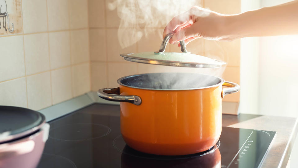 A lid being lifted on a saucepan to release steam while cooking on an electric cooktop