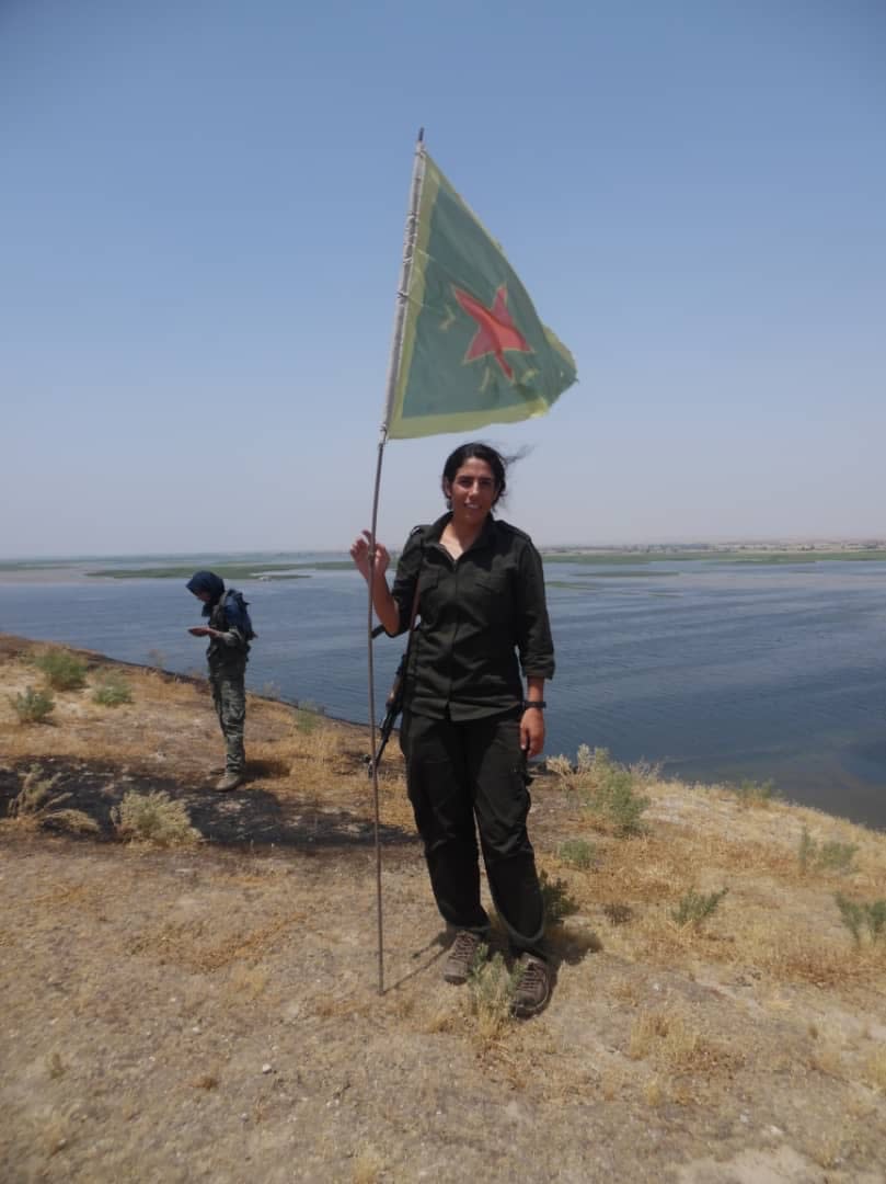 Azeema standing with a flag in the Kobani countryside in Syria, in January 2015.<span class="copyright">Courtesy Mustafa Alali</span>