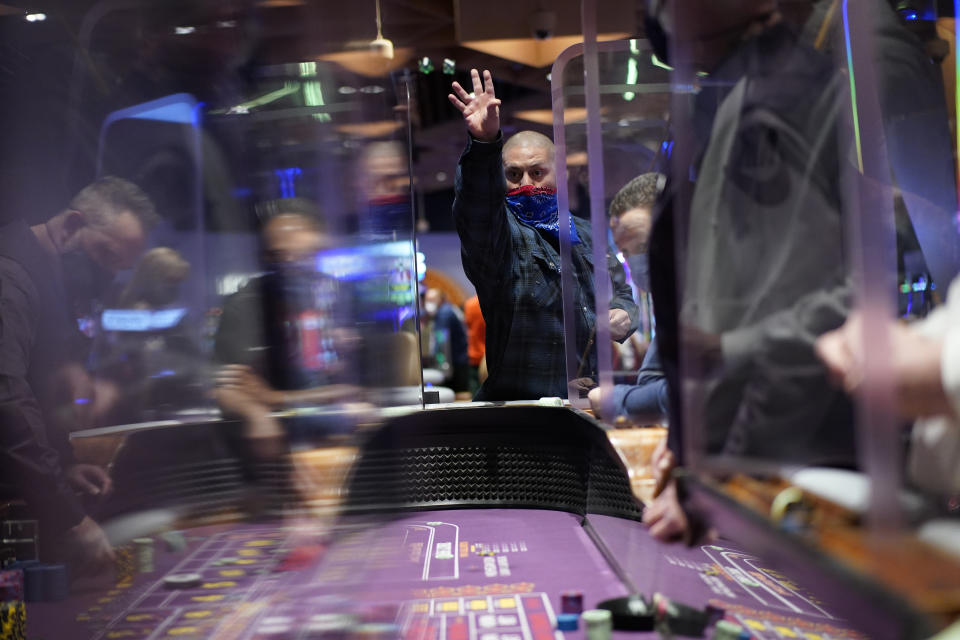 People play craps while wearing masks and between plexiglas partitions as a precaution against the coronavirus at the opening night of the Mohegan Sun Casino at Virgin Hotels Las Vegas, Thursday, March 25, 2021, in Las Vegas. The casino opened at the former Hard Rock Hotel property. (AP Photo/John Locher)