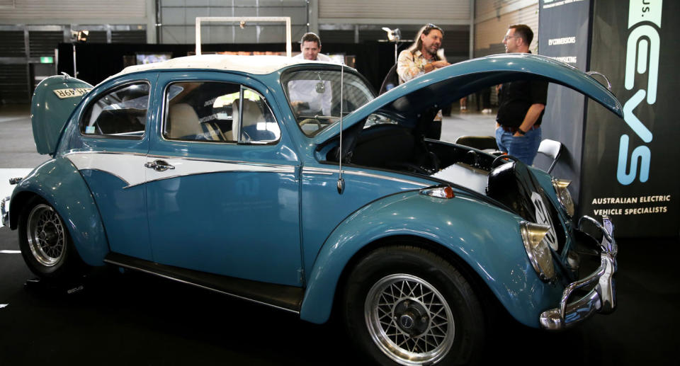 People looking at a vintage looking EV car.