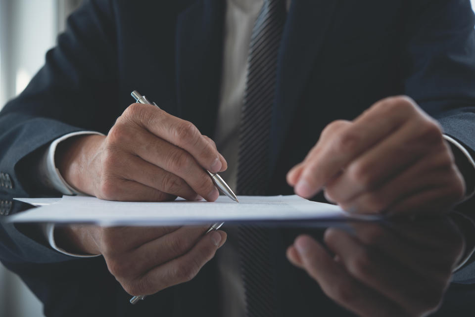 A person in a business suit writing something on a piece of paper