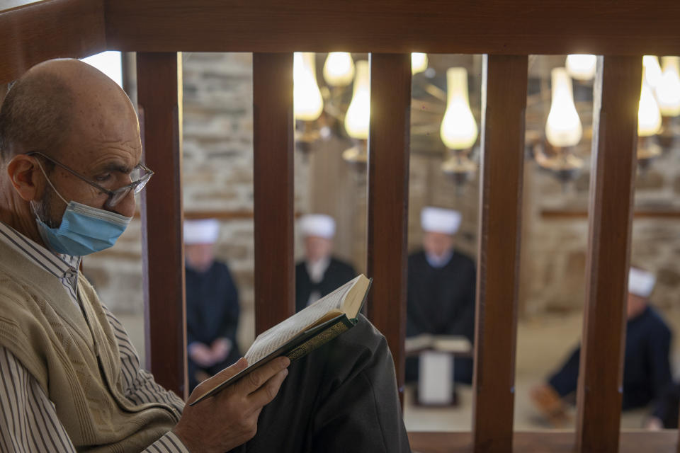 A man reads the Quran as imams attend the Ramadan prayer at a mosque empty of faithful due to social distancing guidelines during the coronavirus outbreak in Zenica, central Bosnia, Thursday, April 23, 2020. The COVID-19 virus pandemic is cutting off the world's Muslims from their cherished Ramadan traditions. (AP Photo/Almir Alic)