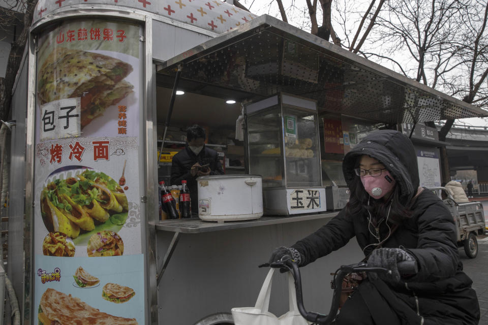 A masked bicyclist passes by a breakfast stand in the central business district in Beijing Monday, March 9, 2020. With almost no new COVID-19 cases being reported in Beijing, workers are slowly returning to their offices with masks on and disinfectant in hand. But officials remain cautious, torn between wanting to restart the economy and fear of a resurgence of the outbreak. (AP Photo/Ng Han Guan)