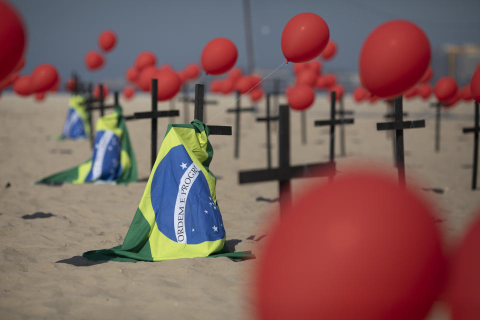 Cruces, globos rojos y la bandera de Brasil son colocados en la playa de Copacabana por el organismo no gubernamental Río de Paz en honor a las víctimas de COVID-19, en Río de Janeiro, Brasil, el sábado 8 de agosto de 2020. (AP Foto/Mario Lobao)