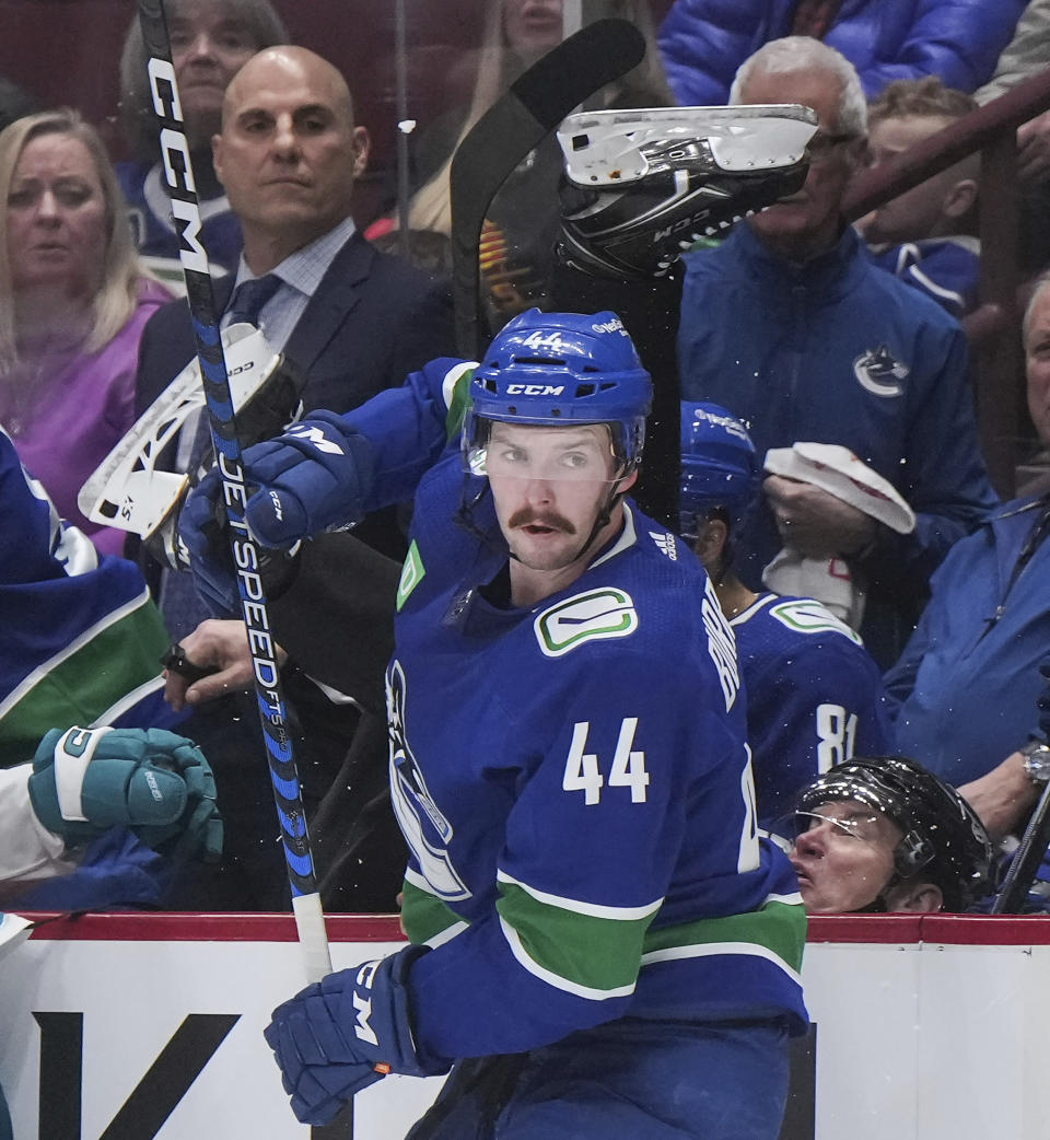 Linesman Scott Cherrey, back right, falls into the Vancouver bench behind Vancouver Canucks' Kyle Burroughs (44) after Burroughs collided with San Jose Sharks' Alexander Barabanov, not seen, during the third period of an NHL hockey game in Vancouver, British Columbia, Thursday, March 23, 2023. (Darryl Dyck/The Canadian Press via AP)