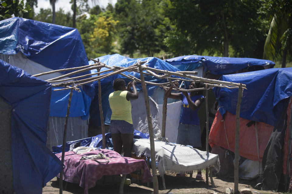 Women left homeless by last year's 7.2-magnitude earthquake create a frame for a makeshift shelter at Camp Devirel in Les Cayes, Haiti, Wednesday, Aug. 17, 2022. A year after the powerful quake hits southern Haiti, the hundreds that were left homeless are still living in tents. (AP Photo/Odelyn Joseph)