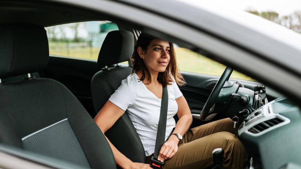 Photo of a business woman sitting in a car putting on her seat belt.