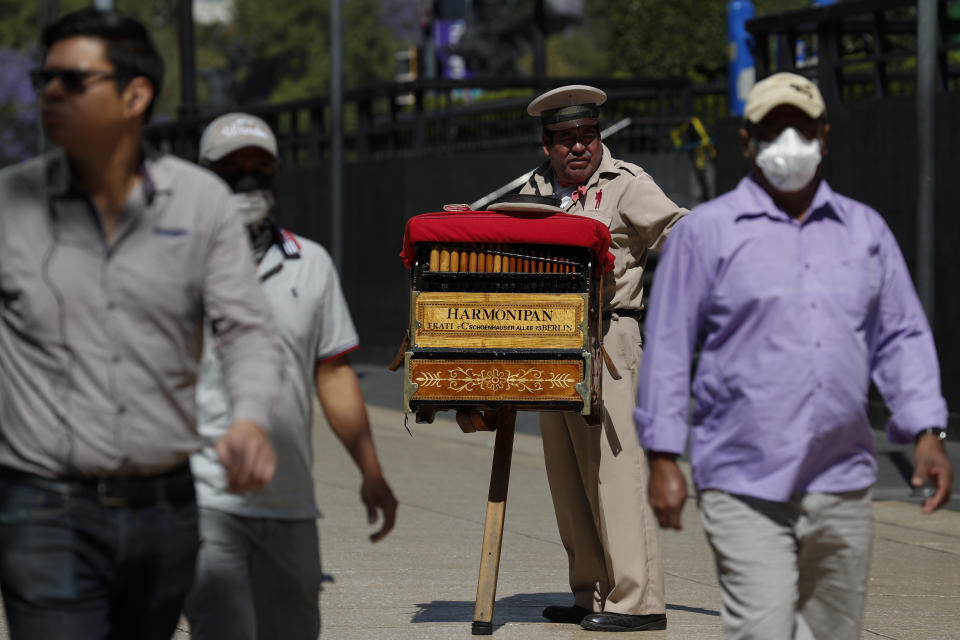 Organ grinder Moises Rosas solicits tips from pedestrians in central Mexico City, Tuesday, March 24, 2020. Rosas, who has been an organ grinder for 25 years, says he isn't afraid of the new coronavirus and needs the average of 200 pesos (around $8.50) he takes home per day. "We live from day to day, so if we don't work, there won't be income for the house, the family." (AP Photo/Rebecca Blackwell)