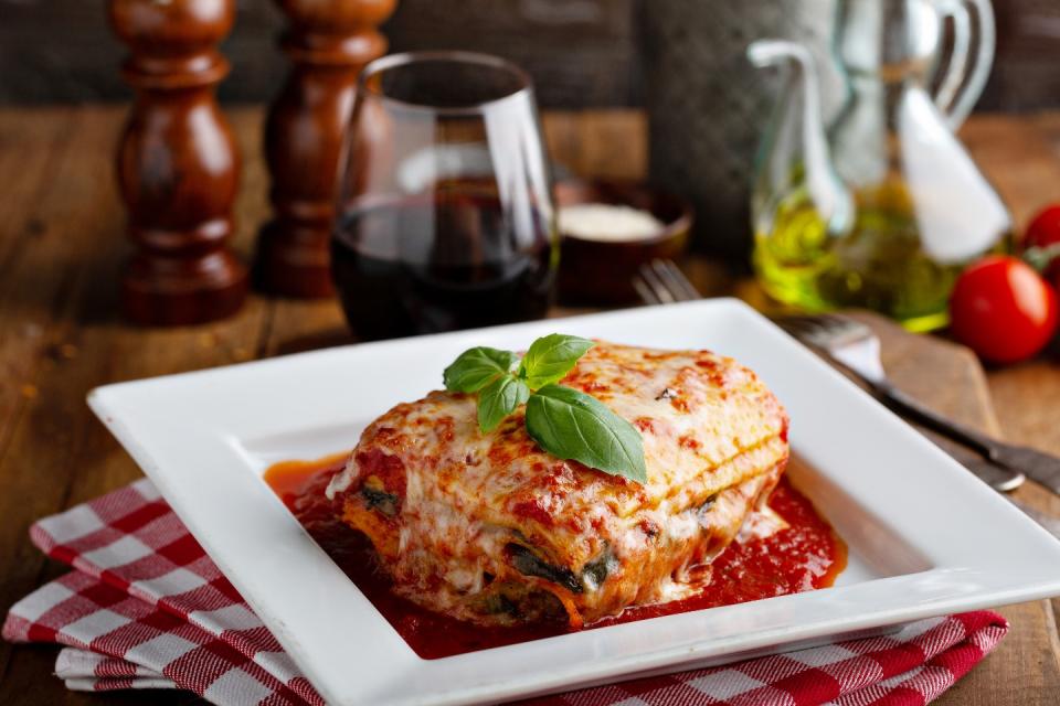 Classic lasagna piece on a plate with basil leaf on top and a glass of red wine.