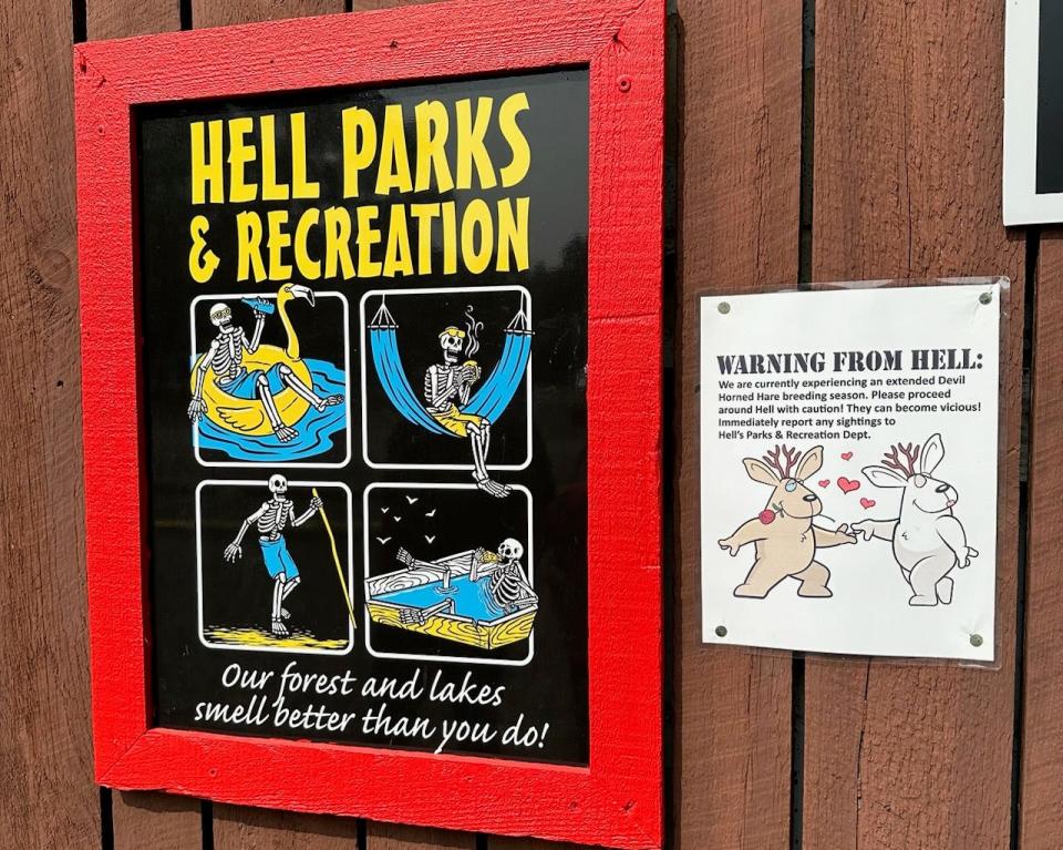Hell Parks and Recreation sign featuring a skeleton in a hammock, a float, and a coffin pool next to a warning about an extended breeding season for devilhorn hares 