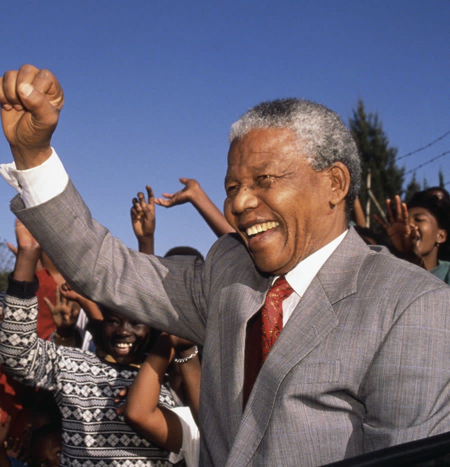 Nelson in a suit and smiling with his fist raised