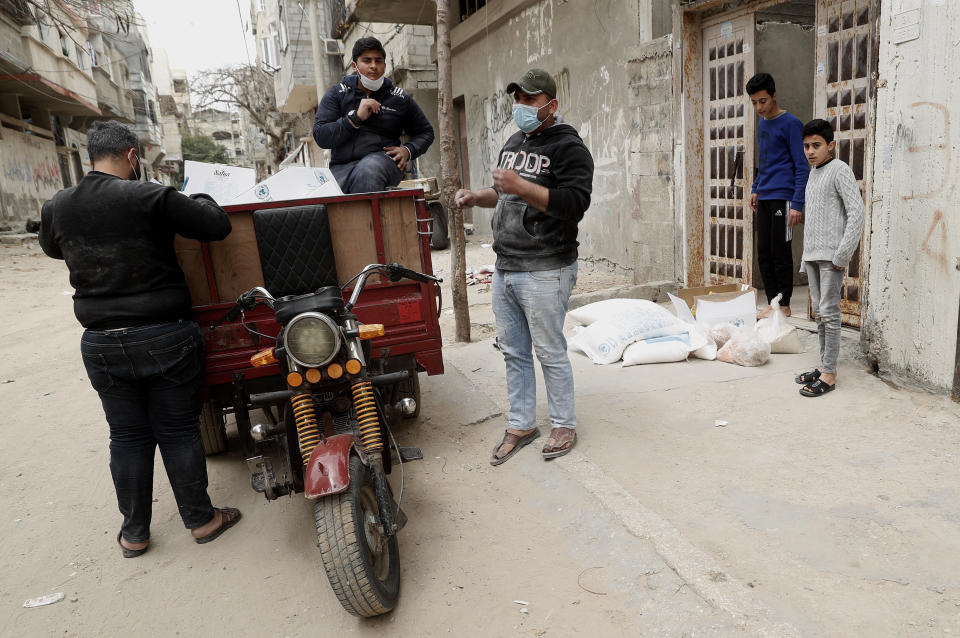 Palestinian workers distribute food supplies from the United Nations Relief and Works Agency (UNRWA) to a house, in the Sheikh Redwan neighborhood of Gaza City, Tuesday, March 31, 2020. The UN has resumed food deliveries to thousands of impoverished families in the Gaza Strip after a three-week delay caused by fears of the coronavirus (AP Photo/Adel Hana)