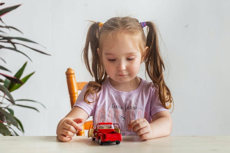 A girl playing with a red toy car.