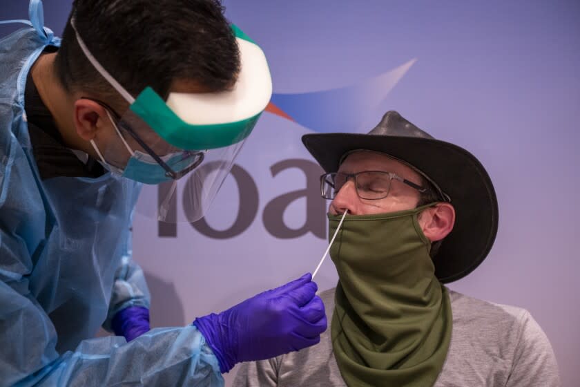 Santa Ana, CA - December 21: Ergee Almalvez, left, licensed vocational nurse, Hoag Memorial Hospital Fly Well Clinic, administers a COVID-19 Rapid PCR test to Kevin Black, of Aliso Viejo, for he and his wife's upcoming trip to London, England, at John Wayne Airport in Santa Ana, CA on Tuesday, Dec. 21, 2021. Travelers arrived and departed for Christmas and holiday travel, although some people are cancelling or rethinking their holiday travel plans because of their fear of contracting the omicron variant. Allen J. Schaben / Los Angeles Times)