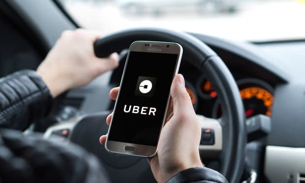 Uber driver holding smartphone in car. Uber is an American company offering transportation services online. Photo: Shutterstock.com.