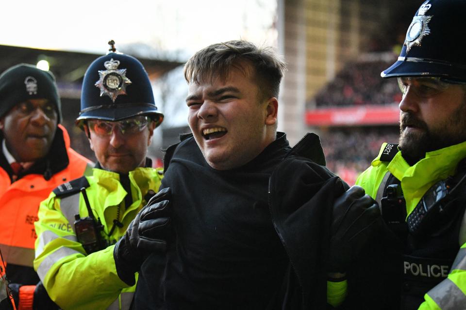 A supporter is taken away by police officers after assaulting Nottingham Forest players as they celebrated their third goal during the English FA Cup fourth round football match between Nottingham Forest and Leicester City at The City Ground in Nottingham, central England, on February 6, 2022. - - RESTRICTED TO EDITORIAL USE. No use with unauthorized audio, video, data, fixture lists, club/league logos or &#39;live&#39; services. Online in-match use limited to 120 images. An additional 40 images may be used in extra time. No video emulation. Social media in-match use limited to 120 images. An additional 40 images may be used in extra time. No use in betting publications, games or single club/league/player publications. (Photo by JUSTIN TALLIS / AFP) / RESTRICTED TO EDITORIAL USE. No use with unauthorized audio, video, data, fixture lists, club/league logos or &#39;live&#39; services. Online in-match use limited to 120 images. An additional 40 images may be used in extra time. No video emulation. Social media in-match use limited to 120 images. An additional 40 images may be used in extra time. No use in betting publications, games or single club/league/player publications. / RESTRICTED TO EDITORIAL USE. No use with unauthorized audio, video, data, fixture lists, club/league logos or &#39;live&#39; services. Online in-match use limited to 120 images. An additional 40 images may be used in extra time. No video emulation. Social media in-match use limited to 120 images. An additional 40 images may be used in extra time. No use in betting publications, games or single club/league/player publications. (Photo by JUSTIN TALLIS/AFP via Getty Images)