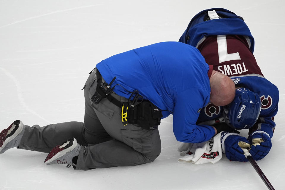Colorado Avalanche defenseman Devon Toews, right, is checked on by head athletic trainer Matthew Sokolowski after Toews took a high stick to the face from Winnipeg Jets center Gabriel Vilardi during the third period of Game 3 of an NHL hockey Stanley Cup first-round playoff series Friday, April 26, 2024, in Denver. (AP Photo/David Zalubowski)