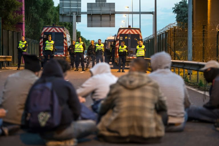 French gendarmes stand facing a group of seated migrants as they block their way in the Eurotunnel site in Coquelles near Calais, northern France, on July 30, 2015