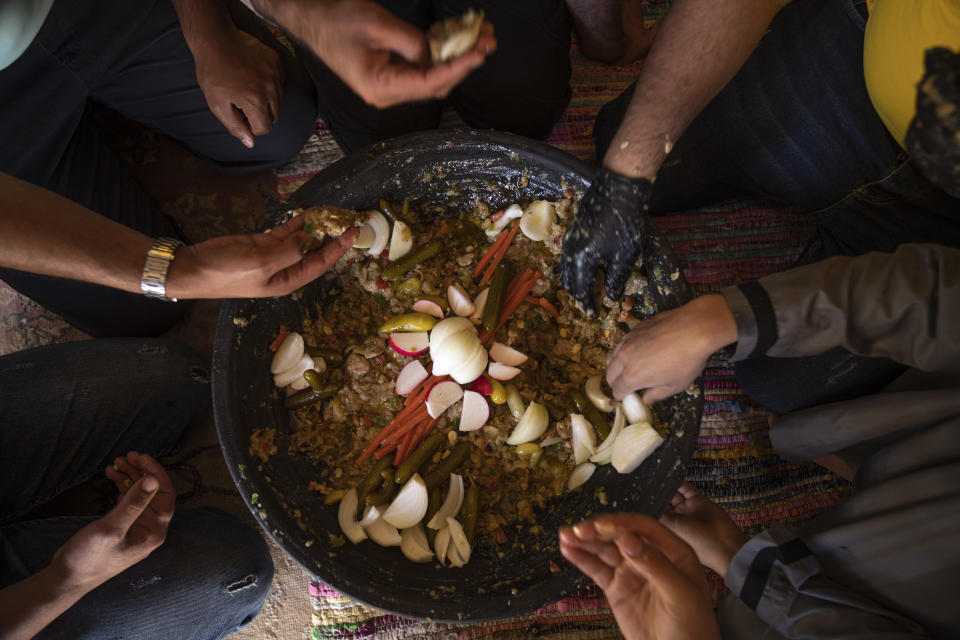 Palestinians eat "Lasima," a dish that is popular in the southern Gaza Strip but shunned in its north, at a garden in Khuzaa, Gaza Strip, Saturday, May 20, 2023. Locals call it "watermelon salad." But this seasonal delicacy is far from the sweet, refreshing taste the name evokes. (AP Photo/Fatima Shbair)