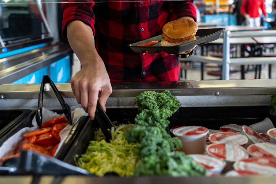 A student gets veggies for his spicy chicken sandwich during lunch at Hamtramck High School in Hamtramck on April 7, 2022.