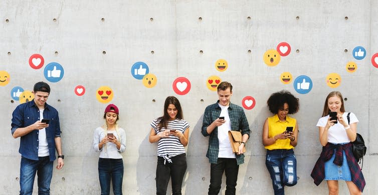 Six young people leaning against a concrete wall, all watching their mobile phones. Emoji icons are emanating from the screens.